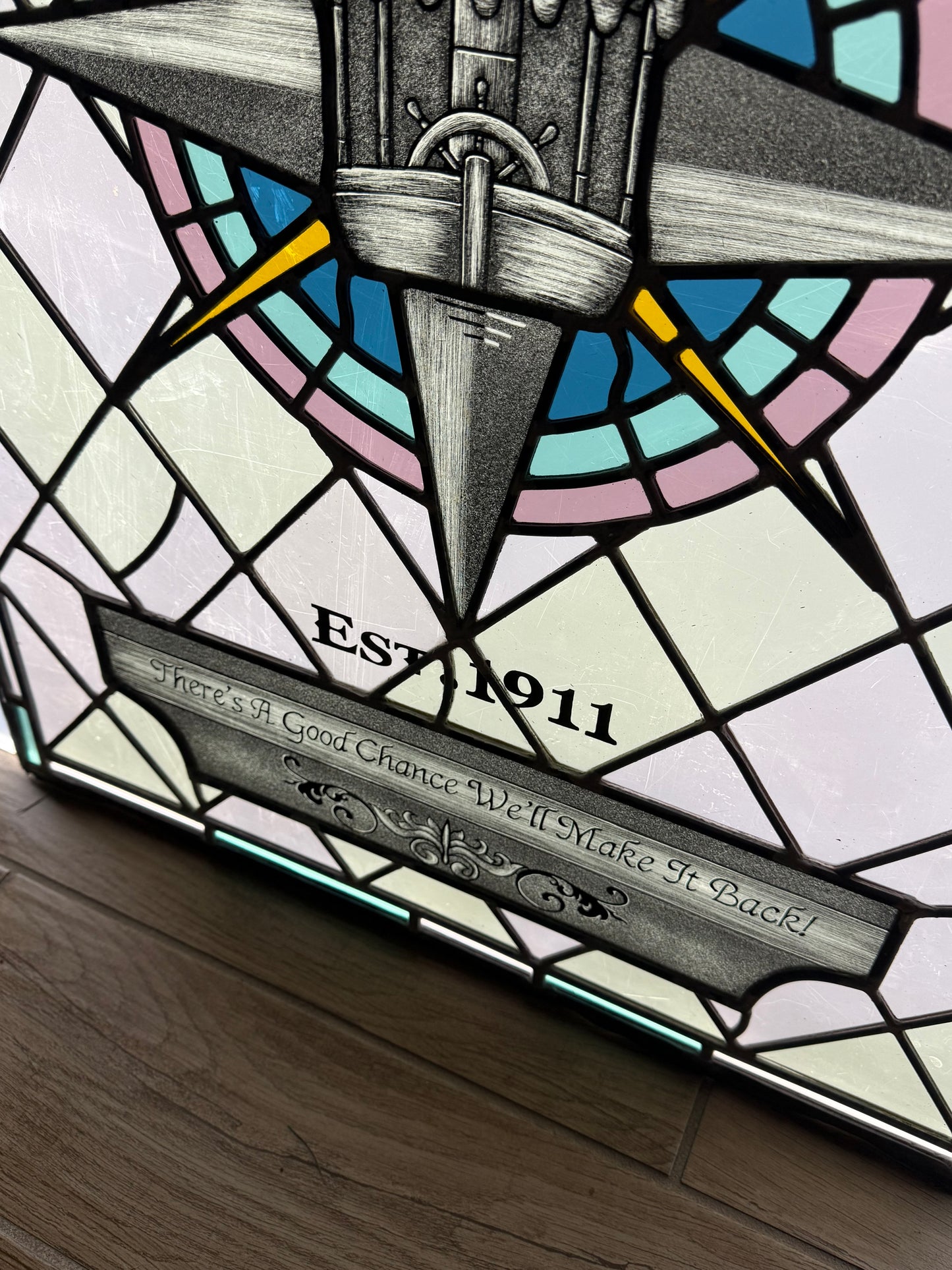 Stained glass panel with compass design and text. Disney Jungle Navigation Company symbol. "Est. 1911" text with "There's a good chance we'll make it back!" text