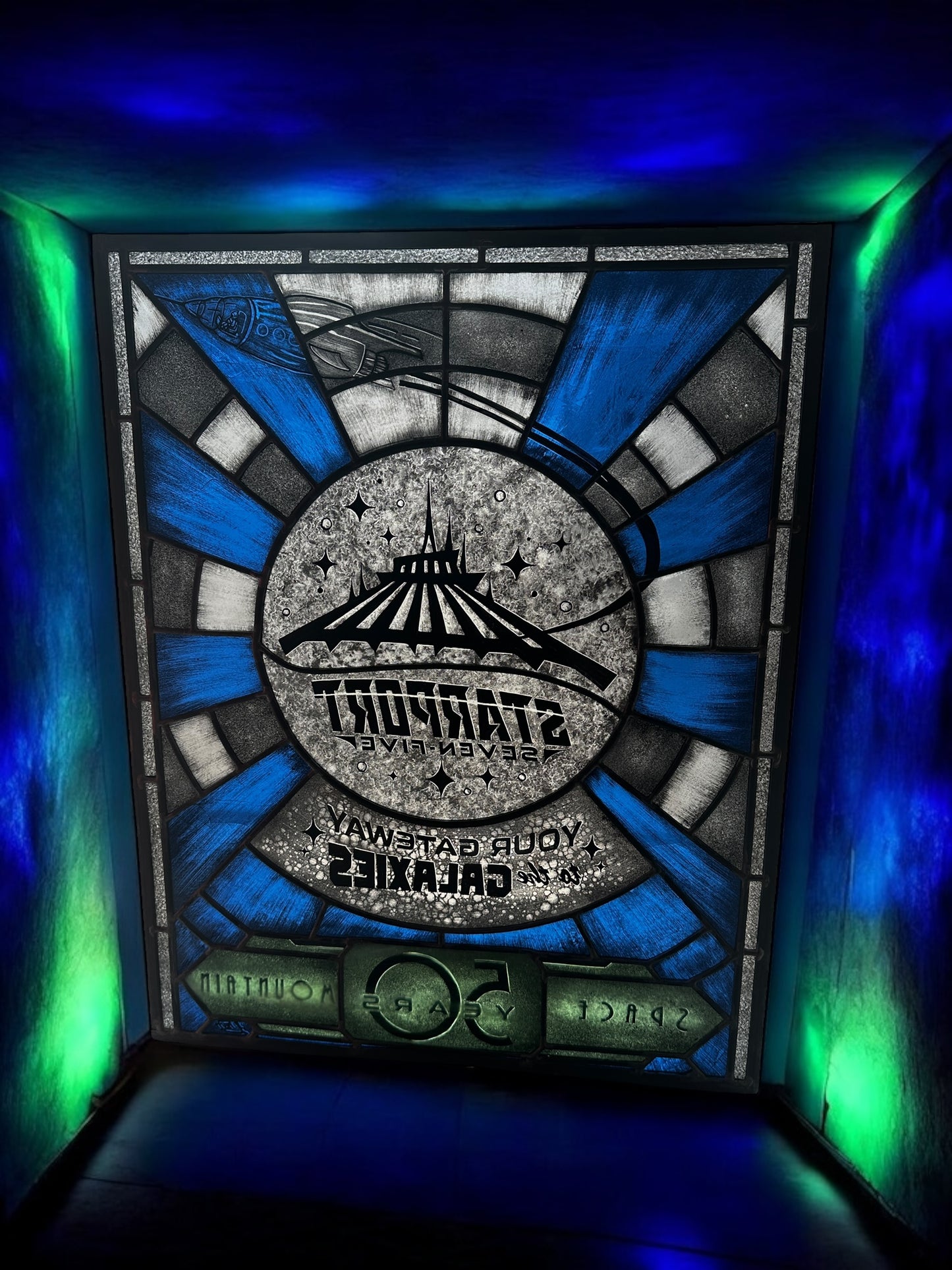 Stylized sign with 'Starport Seven Five' design, stained glass. Blue and white launch tunnel background. '50 years Space Mountain' text. rocket with astronaut blasting off. 'Your Gateway to the Galaxies' text.