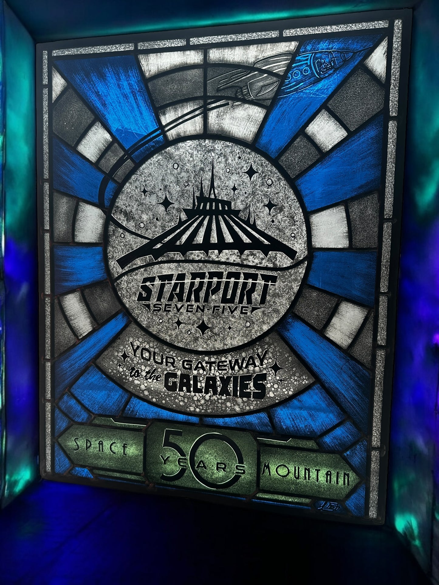 Stylized sign with 'Starport Seven Five' design, stained glass. Blue and white launch tunnel background. '50 years Space Mountain' text. rocket with astronaut blasting off. 'Your Gateway to the Galaxies' text.