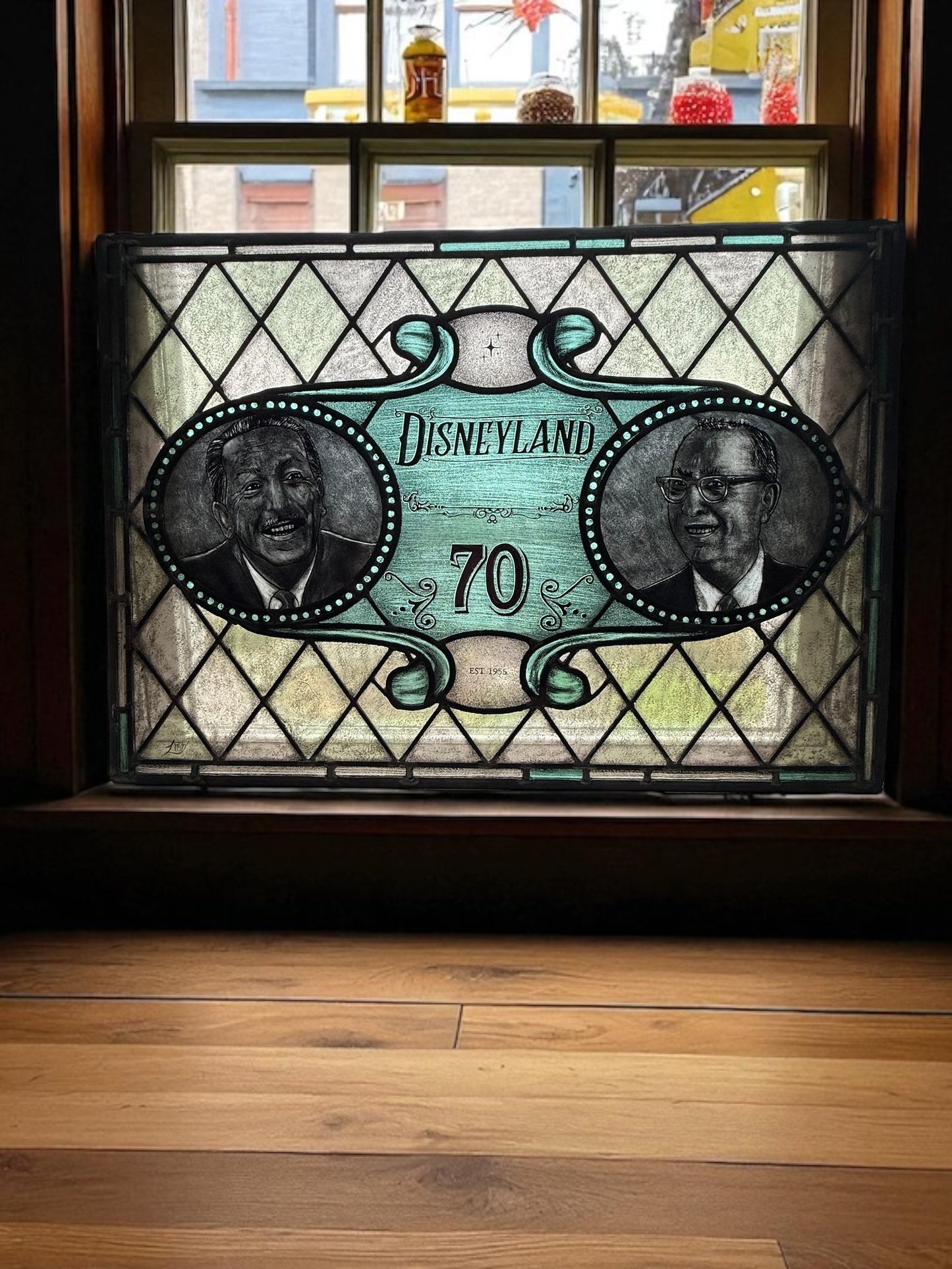 Decorative stained glass panel with 'Disneyland 70' and portraits on a wooden window surface. Walt and Roy Disney faces.