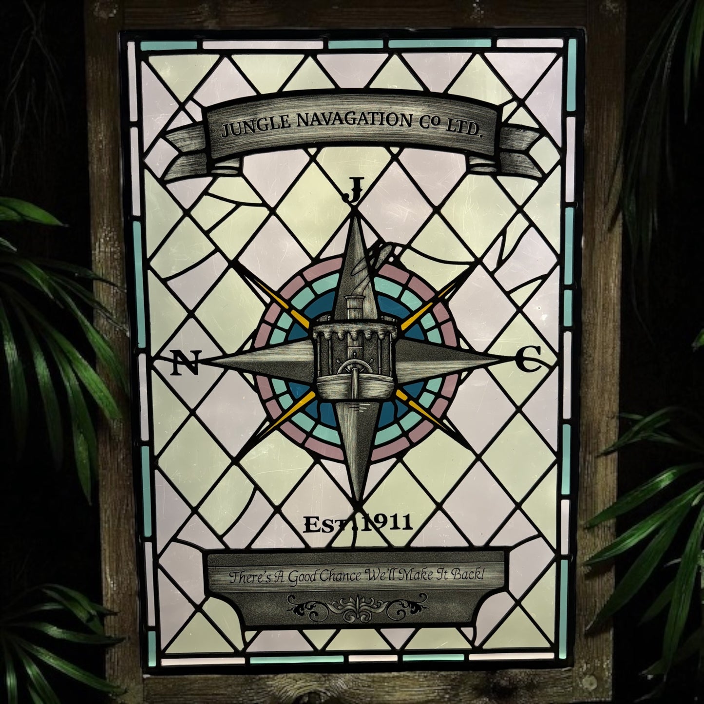 Stained glass panel with compass design and text, framed by green foliage. Disney Jungle Navigation Company
