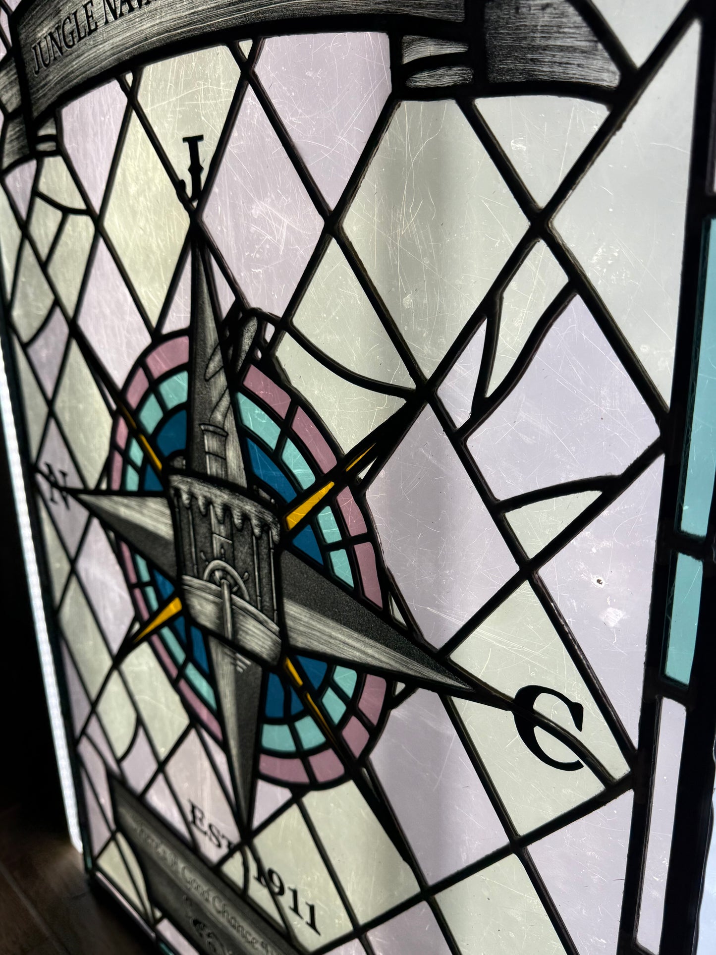 Stained glass panel with compass design and text. Disney Jungle Navigation Company symbol