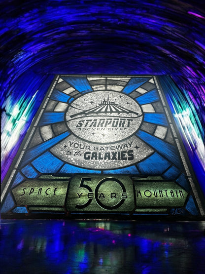 Stylized sign with 'Starport Seven Five' design,  stained glass. Blue and white launch tunnel background. '50 years Space Mountain' text. rocket with astronaut blasting off. 'Your Gateway to the Galaxies' text.