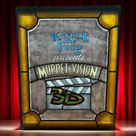 Decorative stained glass panel with 'Kermit the Frog presents Muppet Vision 3D' text against a red curtain with spotlight background