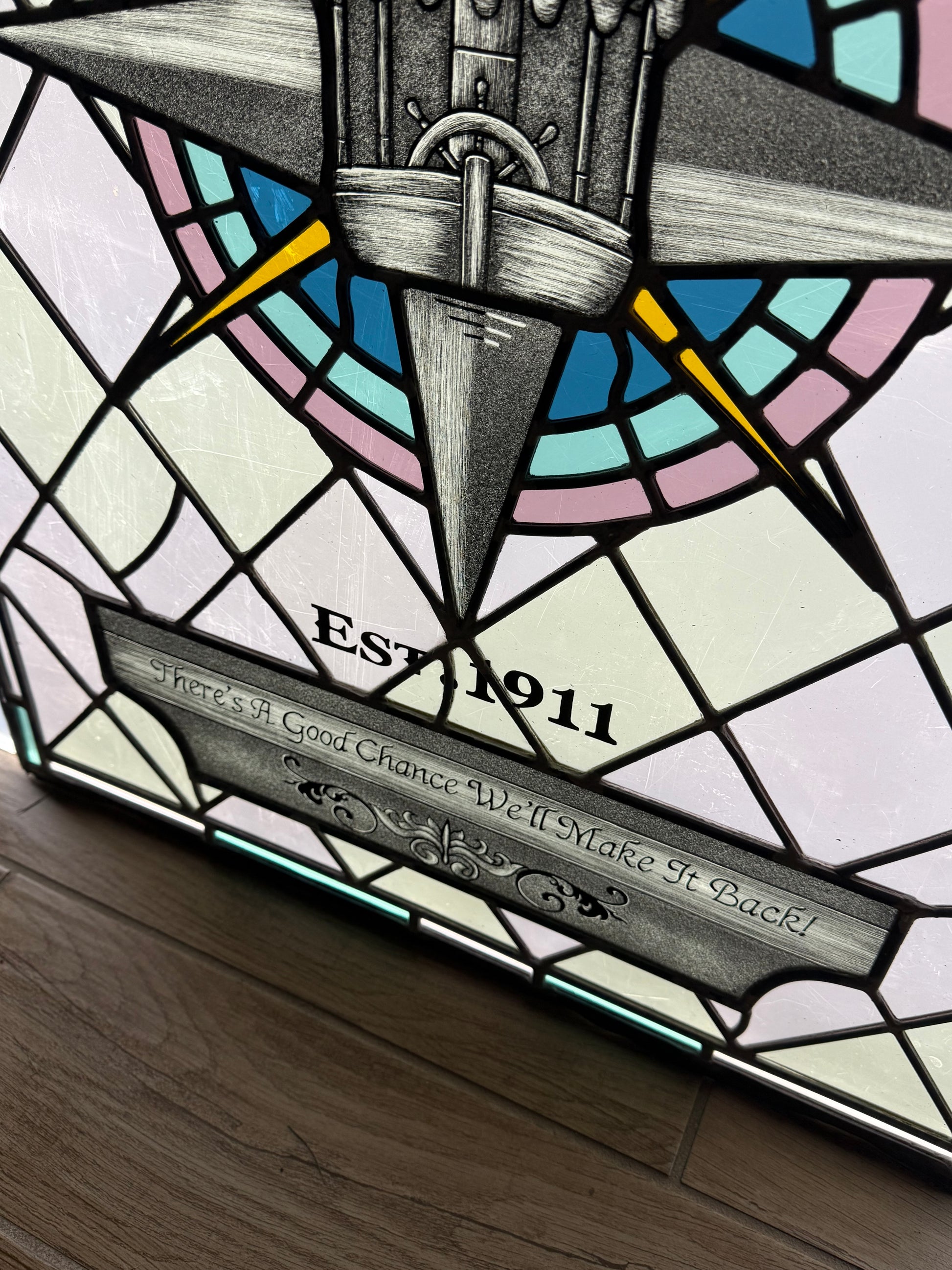 Stained glass panel with compass design and text. Disney Jungle Navigation Company symbol. "Est. 1911" text with "There's a good chance we'll make it back!" text