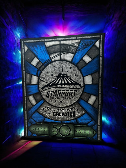 Stylized sign with 'Starport Seven Five' design,  stained glass. Blue and white launch tunnel background. '50 years Space Mountain' text. rocket with astronaut blasting off. 'Your Gateway to the Galaxies' text.