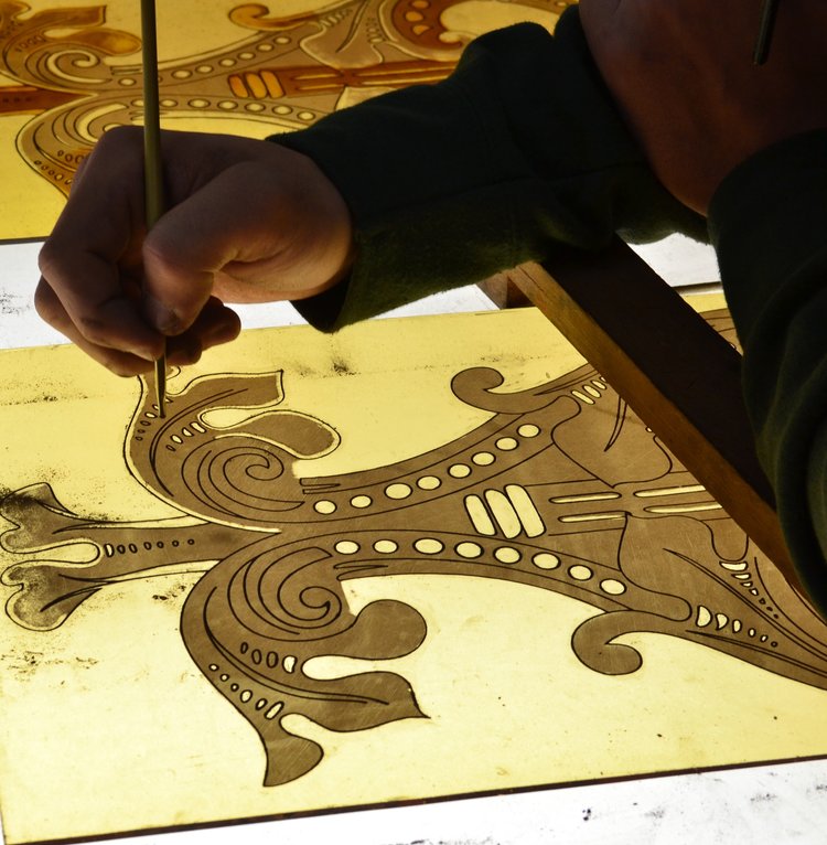 Person painting on a detailed design with a brush on a stained glass surface